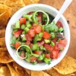 overhead shot of homemade asparagus tomato salsa in a white bowl surrounded by tortilla chips